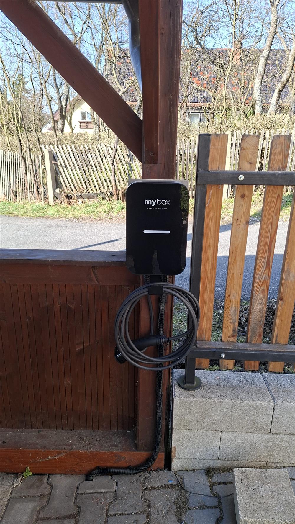 Černý wallbox Mybox s kabelem na dřevěném sloupku u oplocení