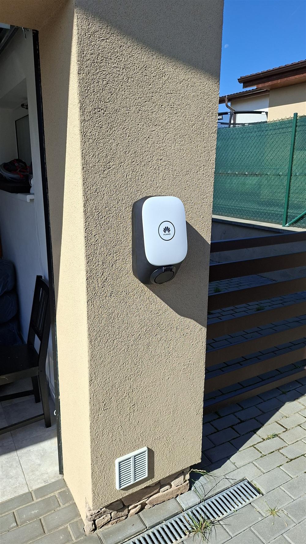 Bílý wallbox Huawei namontovaný na venkovní stěně domu